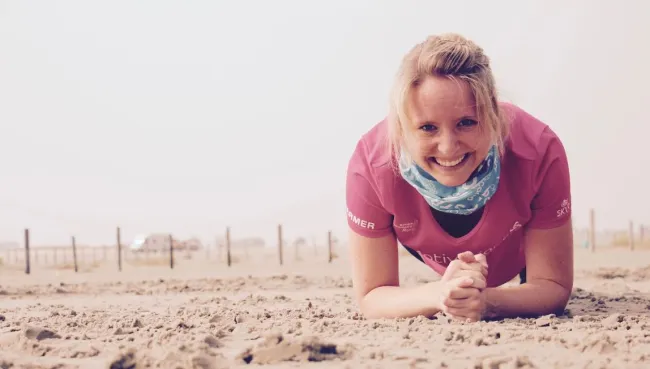 Frau macht Liegestützen am Strand und lächelt dabei