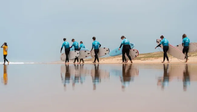 Anfänger:innen gehen in einem Surfcamp in Frankreich gemeinsam mit ihren Surfboards zum Strand