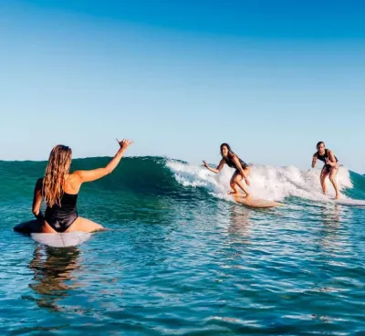 Zwei Freunde teilen sich beim Surfen eine Welle und jubeln ihrer dritten Freundin zu