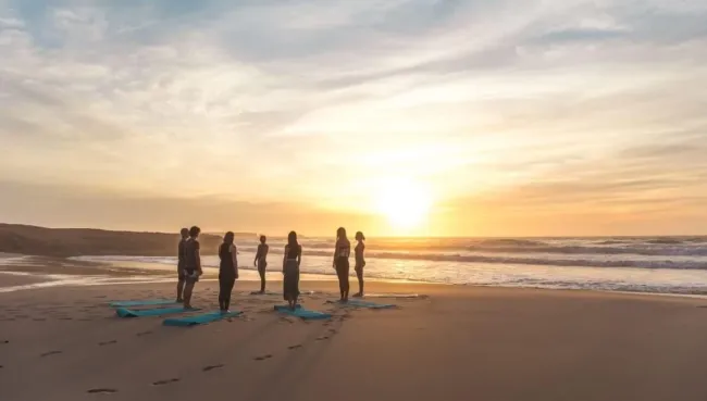 Gruppe beim Yoga am Strand bei Sonnenuntergang