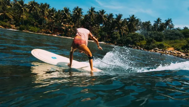 Anfängerin surft in Sri Lanka vor tropischer Küste mit Palmen
