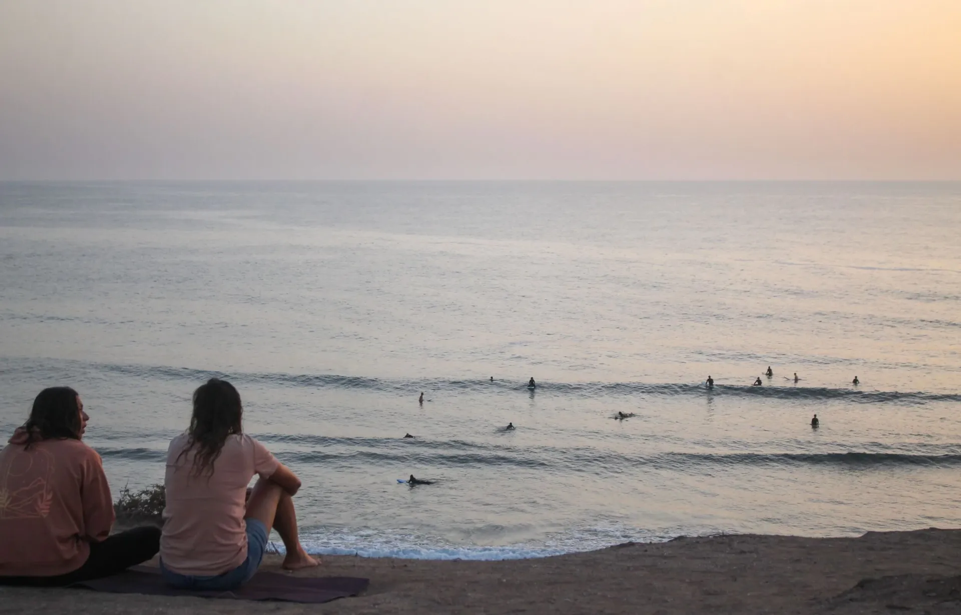 Zwei Freundinnen beobachten von den Klippen in Taghazout die Surfer in den Wellen