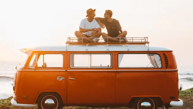 Zwei Freunde sitzen auf ihrem VW-Bus mit Blick auf den Ozean in Portugal