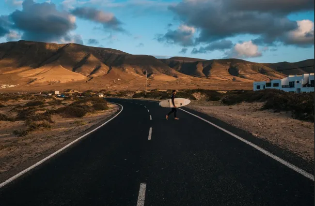 Mann mit Surfboard läuft über Straße auf Lanzarote