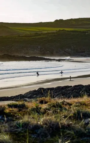 Drei Surfer laufen am einsamen Strand in Asturien in die Wellen