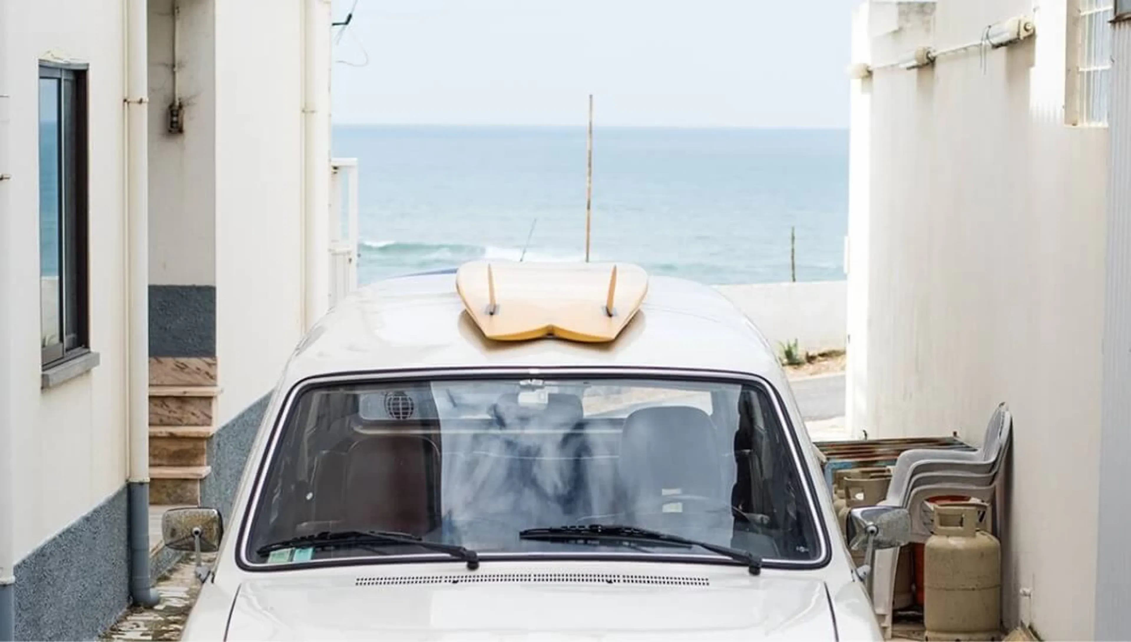 Alter Mercedes mit Surfboard auf dem Dach parkt in den Gassen in Ericeira mit Blick aufdie Wellen