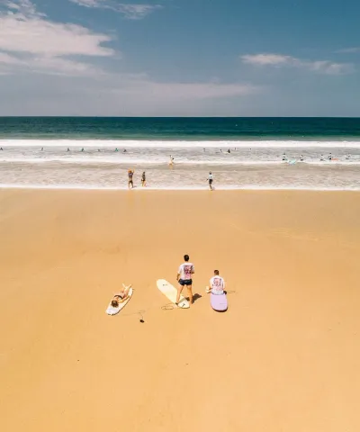 Drei Surfer liegen mit ihren Surfboards am weiten Sandstrand von Moliets und schauen auf die Wellen