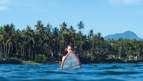 Frau sitz im Ozean auf ihrem Surfboard vor tropischer Kulisse in Costa Rica