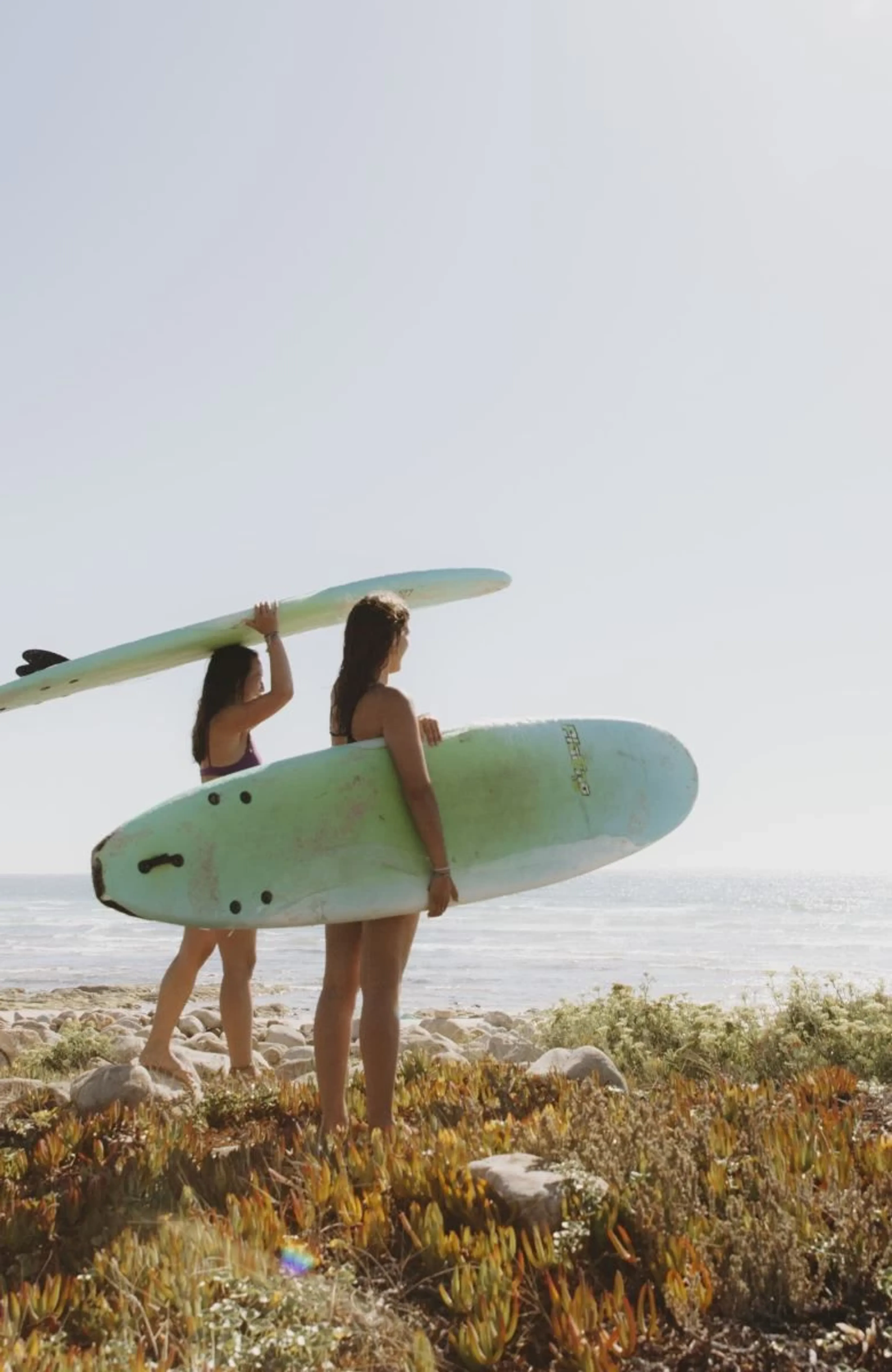 Zwei Freundinnen mit ihren Surfboards schauen von der Klippe auf den Ozean