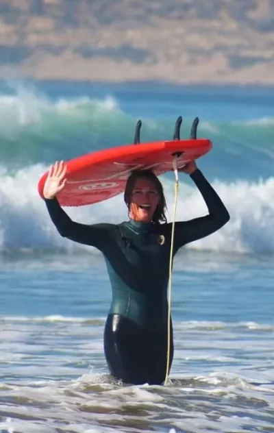 Surf-Anfängerin kommt mit Surfboard aus den Wellen und strahlt