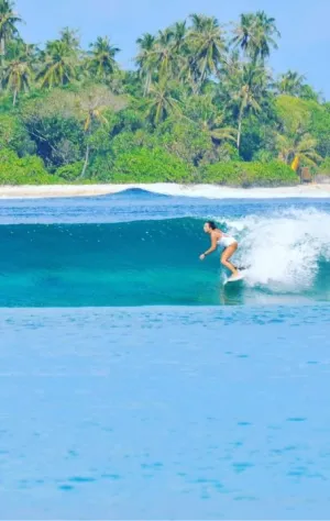 Surferin in cleaner Welle vor tropischer Kulisse auf den Malediven