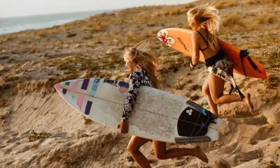 Zwei Surferinnen laufen mit ihren Surfboards vom Surfcamp in Frankreich über die Dünen an den Strand