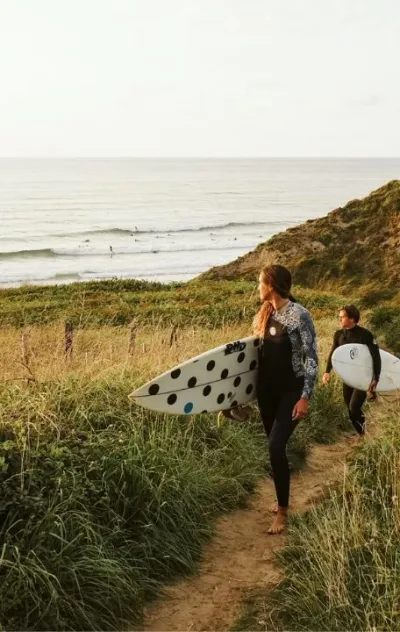 Zwei Surfer laufen mit ihren Surfboards vom grünen Strand in Nordspanien zurück zum Surfcamp