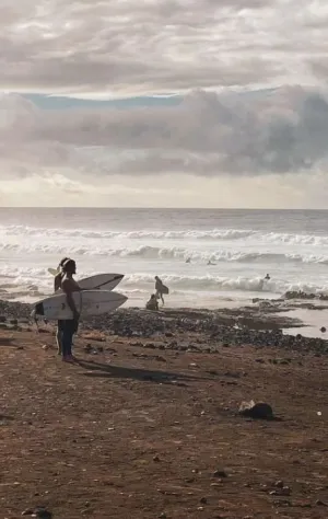 Zwei Surfer stehen mit ihren Surfboards am Strand auf Teneriffa und schauen auf die Wellen