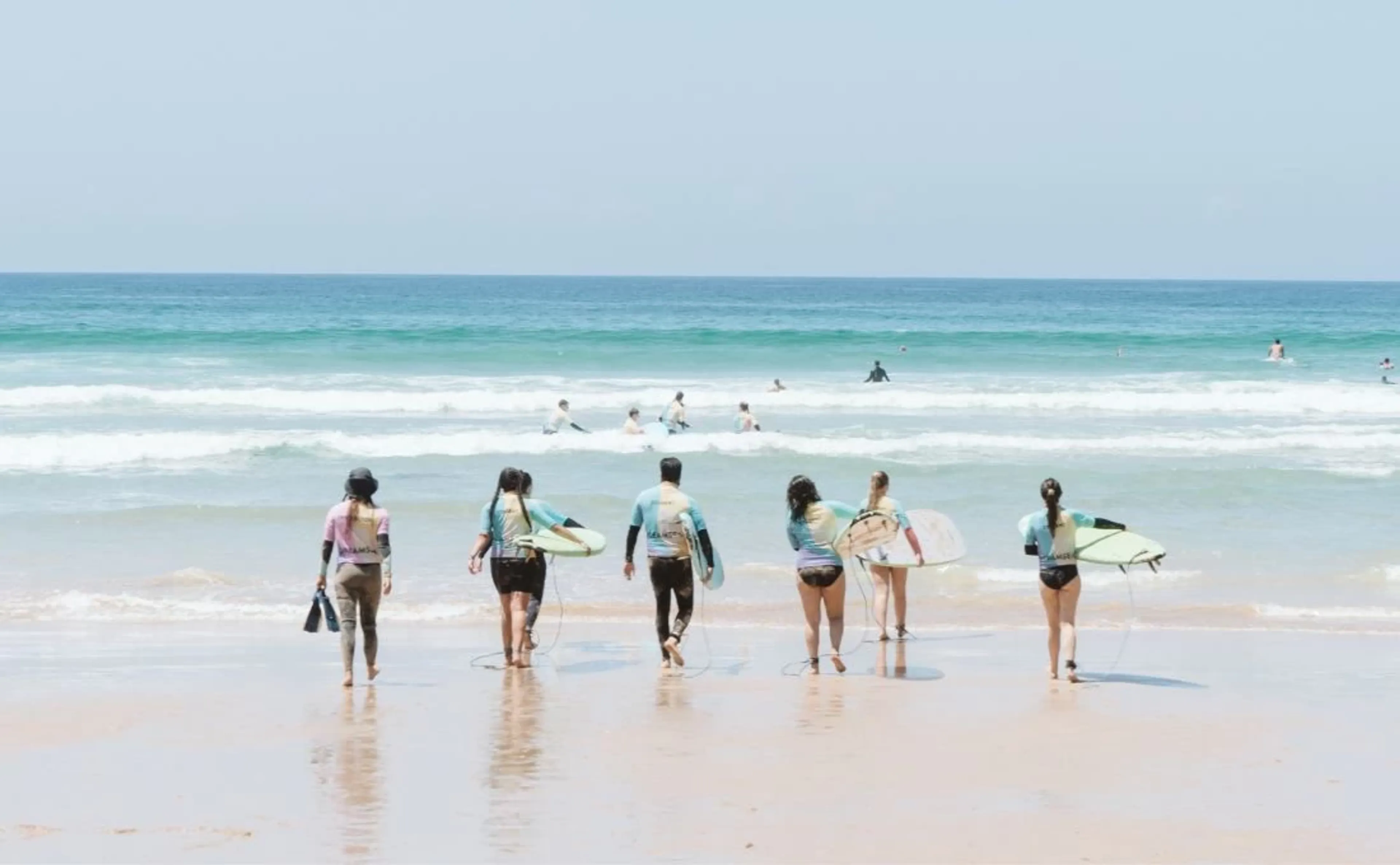 Surfcamp Gruppe geht mit Surfboards vom Strand in die Wellen