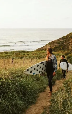 Zwei Surfer laufen mit ihren Surfboards vom Strand zurück und schauen auf die Wellen