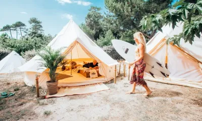 Frau mit Surfboard auf dem Weg zu ihrem Zelt im Surfcamp auf dem Campingplatz in Frankreich