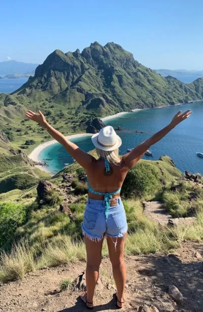 Frau mit hochgestreckten Armen mit Blick auf das Meer