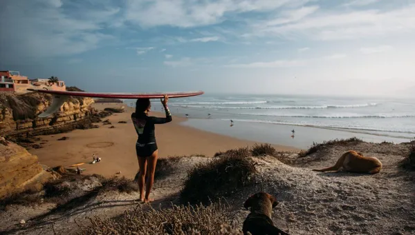 Frau mit Longboard auf dem Weg zum Strand in Marokko mit Blick auf die Wellen