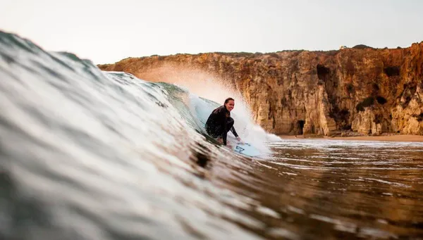 Frau surft cleane Welle mit Klippen im Hintergrund an der Algarve